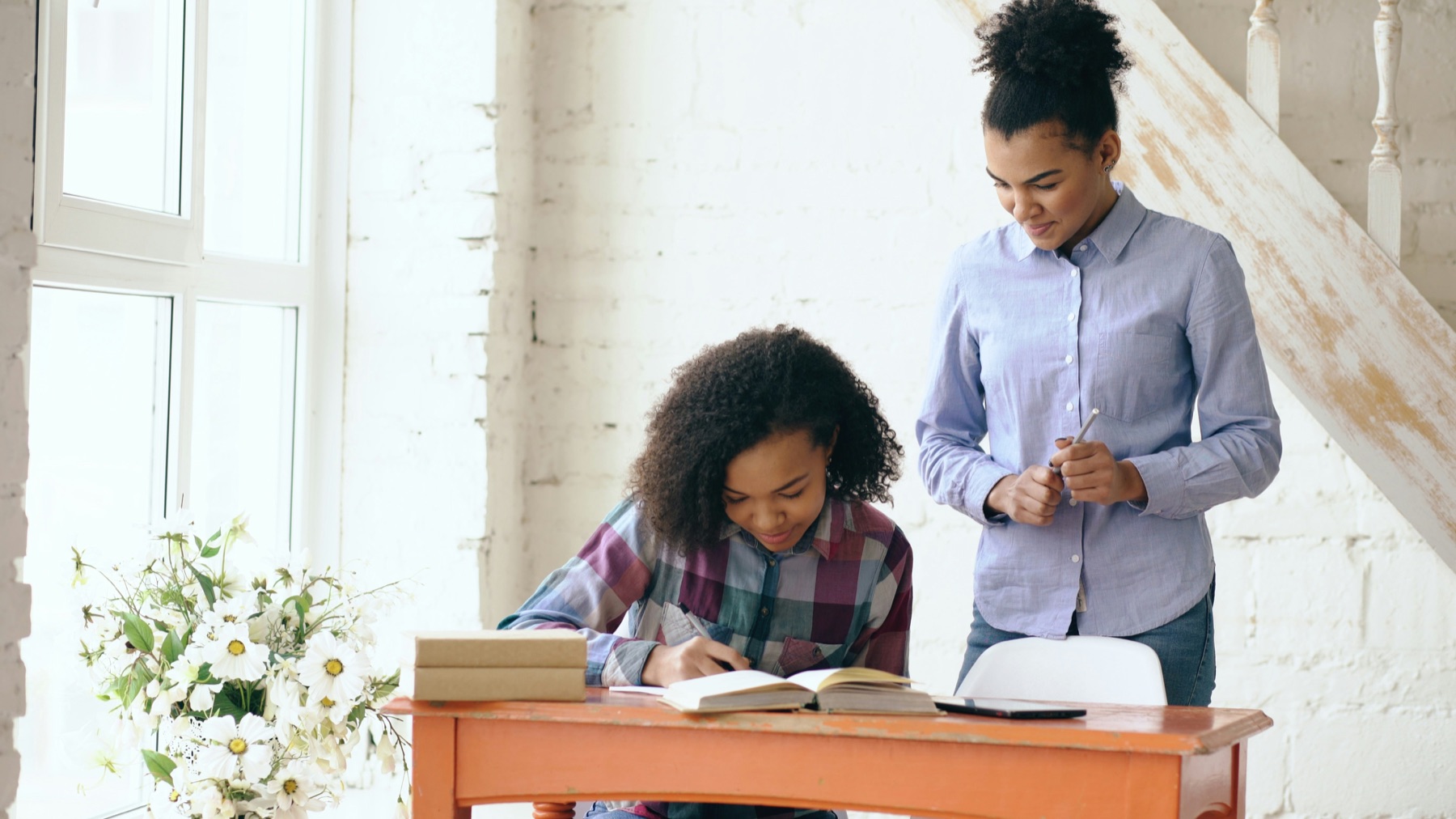 A tutor guiding a student through her homework at a bright desk